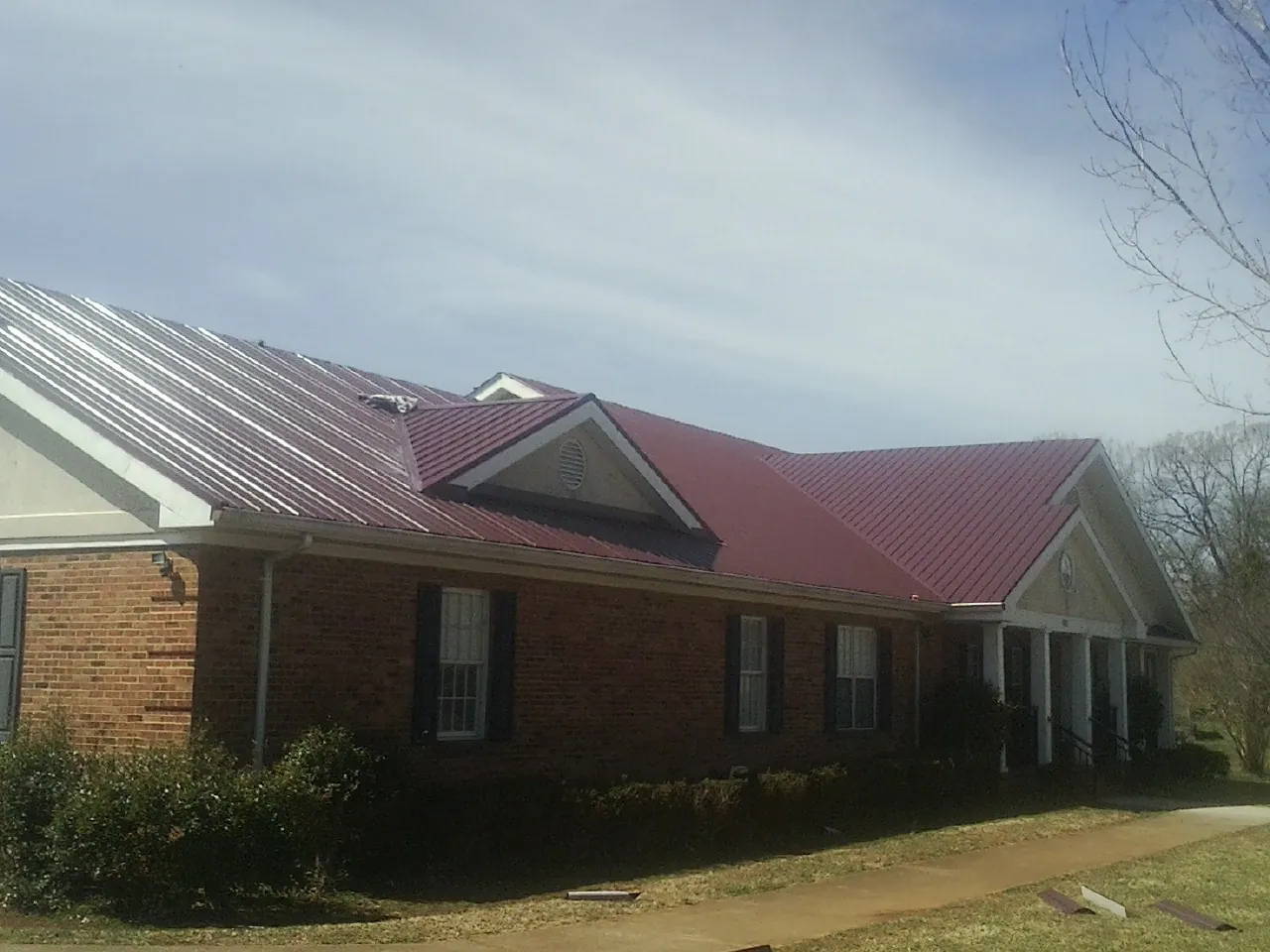 Red metal roof with gabled entries on a long brick building, from a Hail Damage Roof Repair job in Jbsa Lackland