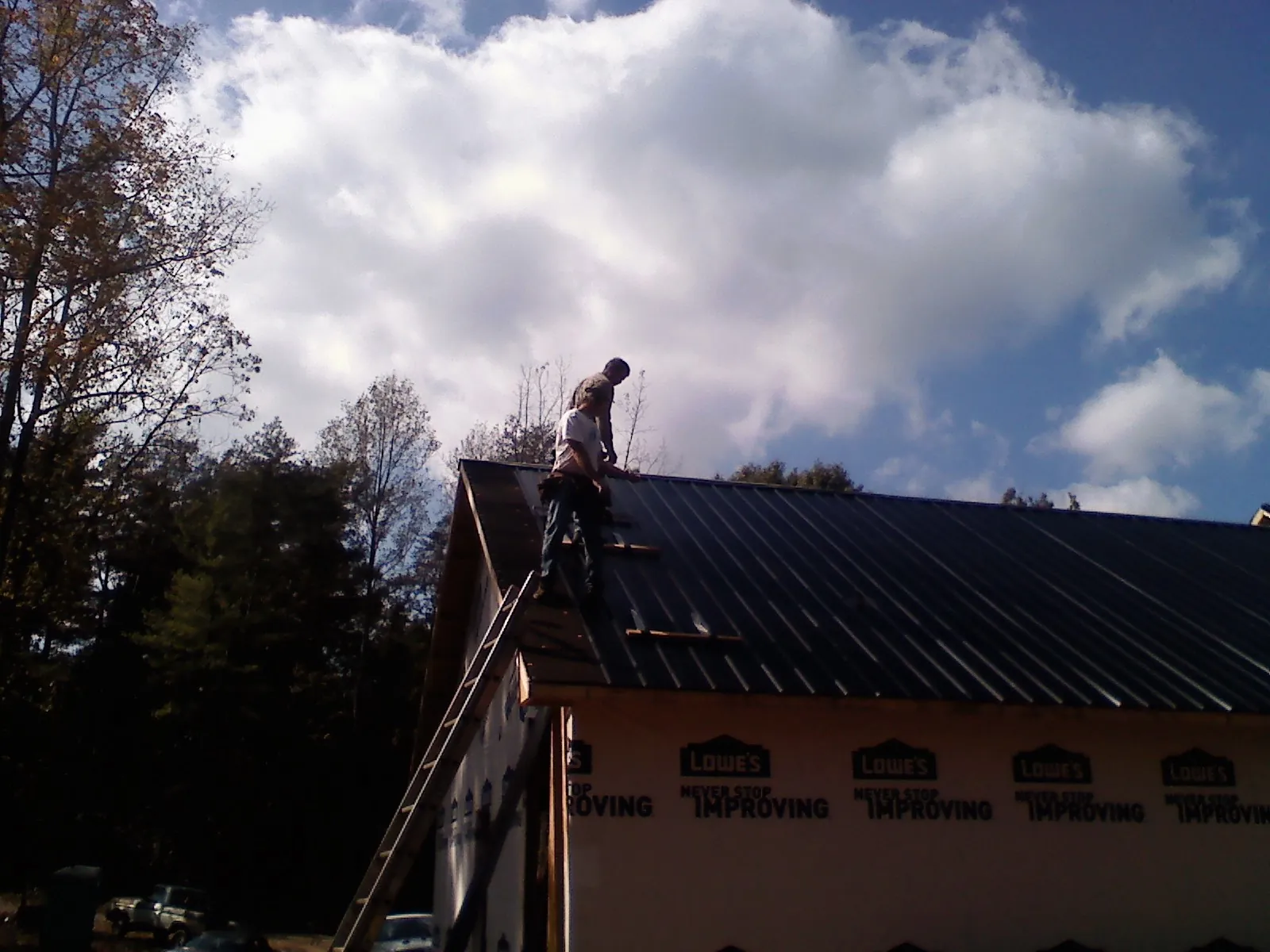 Roofer fastening dark metal panels high against a cloudy sky, from a Roof Inspection job in Jbsa Lackland