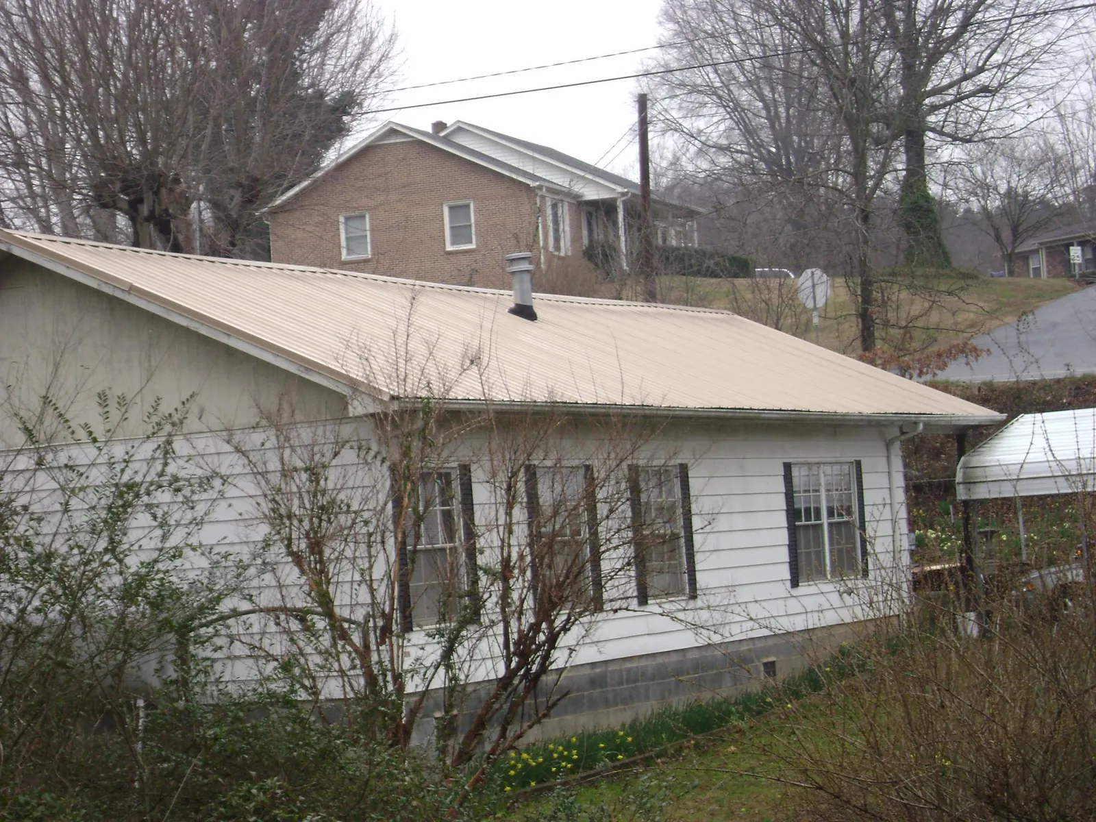 Tan metal roof on a white sided house set into a hillside — Commercial Roofing by Roofing Brothers in Jbsa Lackland