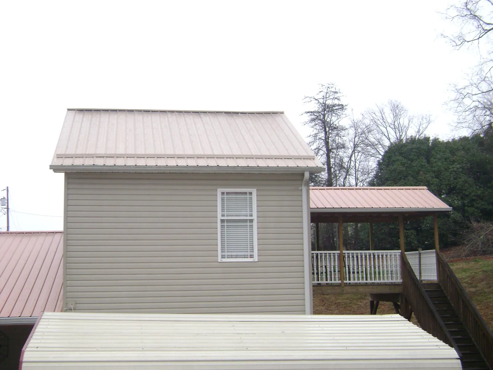 Tan metal roofs on a two story addition and attached porch, from a Roof Replacement job in Jbsa Lackland